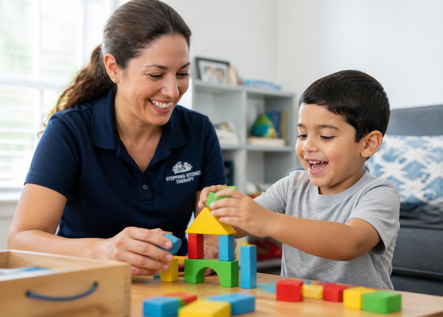A therapist and a young boy building with colorful blocks at home